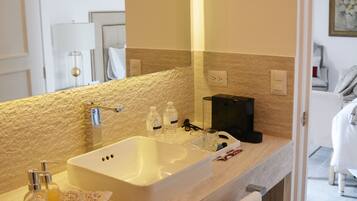 A bathroom with a large mirror, a sink, and a coffee maker. There is a towel hanging on the wall and a tray with toiletries on the counter.
