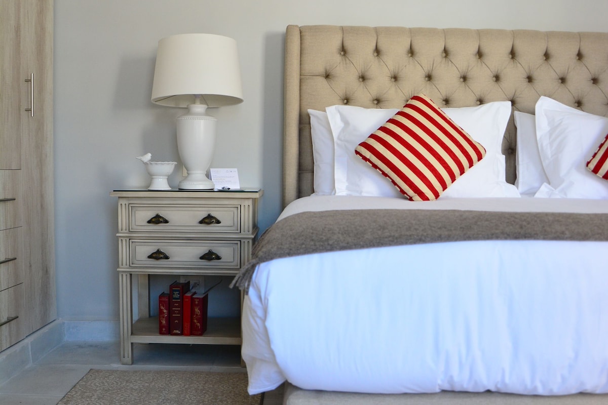 A neatly arranged bedroom with a bed, a nightstand with a lamp, and a small shelf.