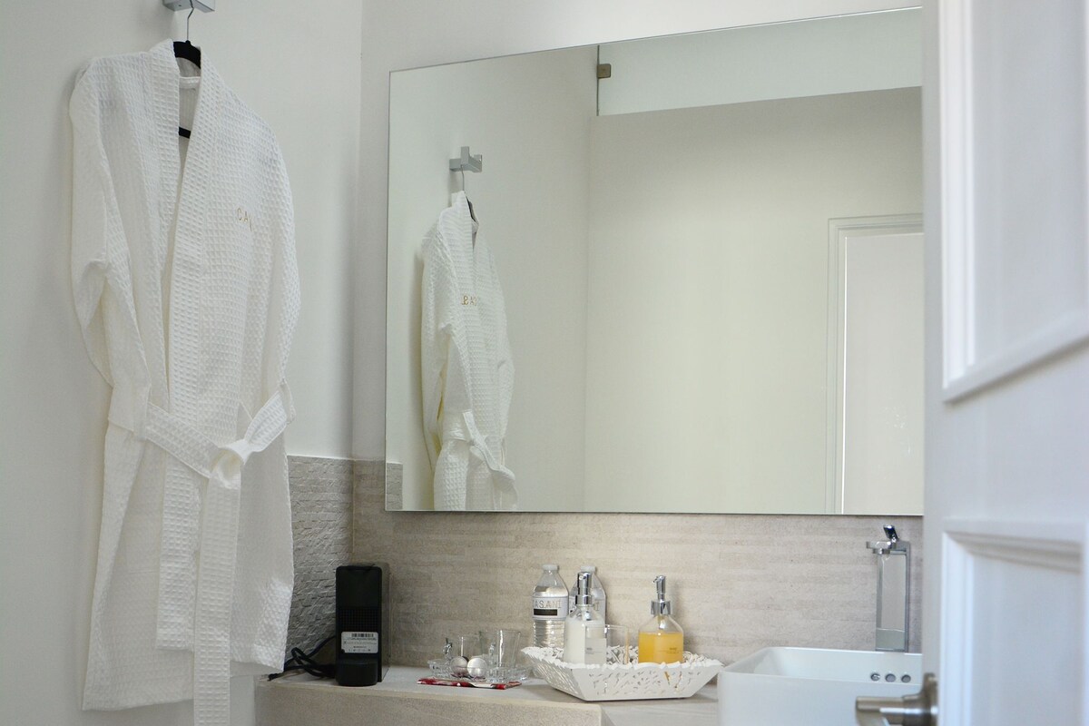 Un baño con inodoro, lavamanos, espejo, toallero y un cubo de basura.