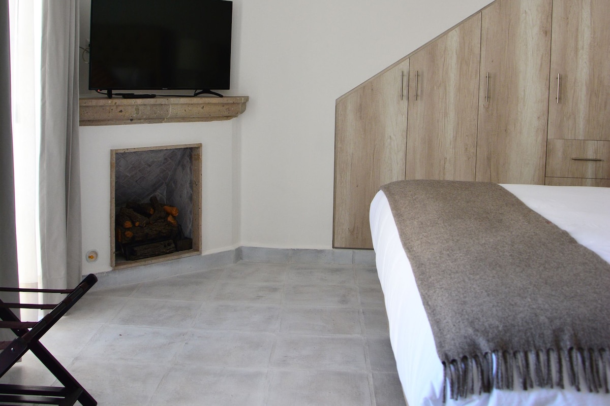 A bedroom with a bed, a TV mounted on a wooden shelf above a fireplace, and a wooden wardrobe.