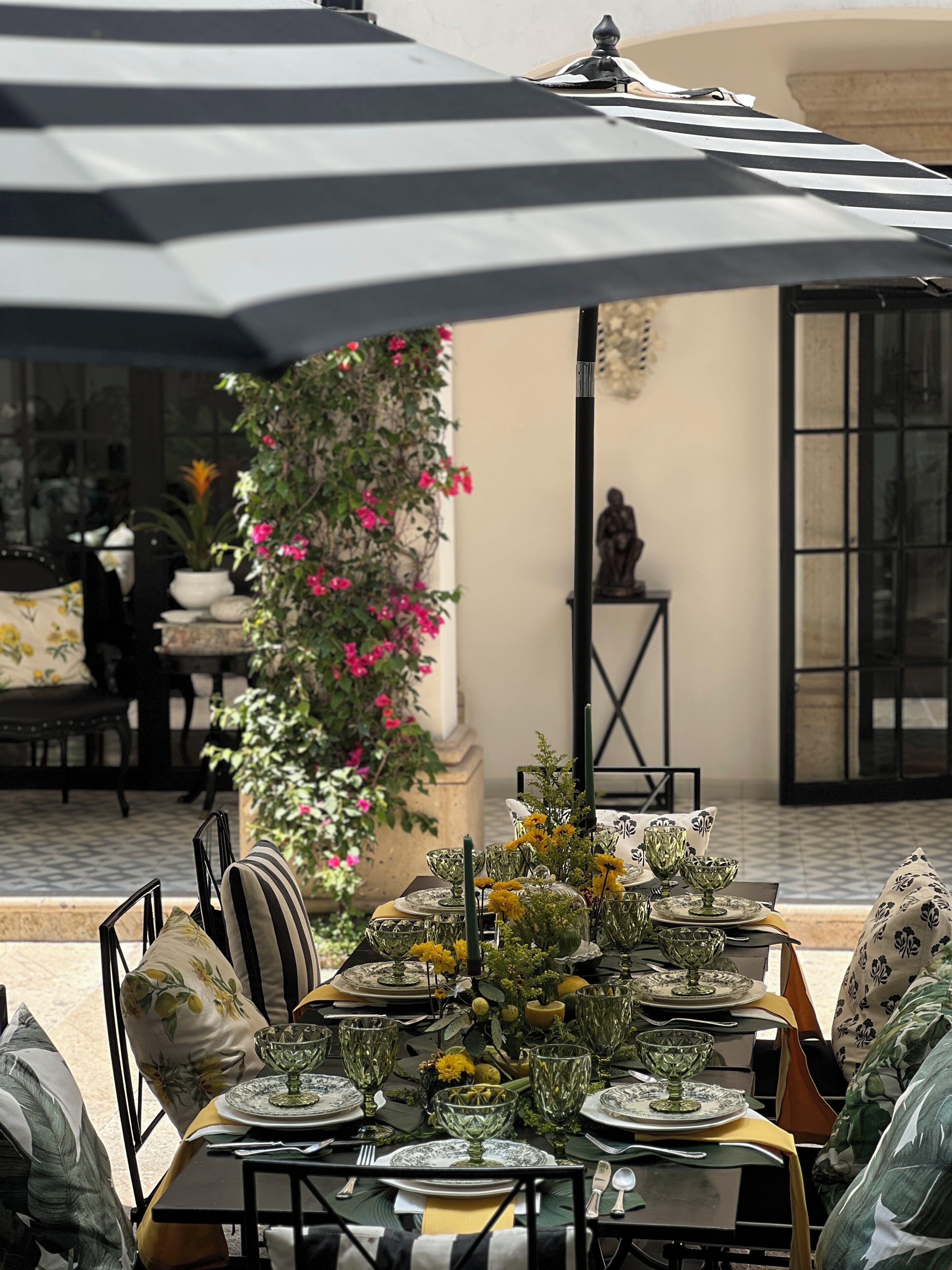 An outdoor dining area with tables set for a meal, surrounded by umbrellas and potted plants.