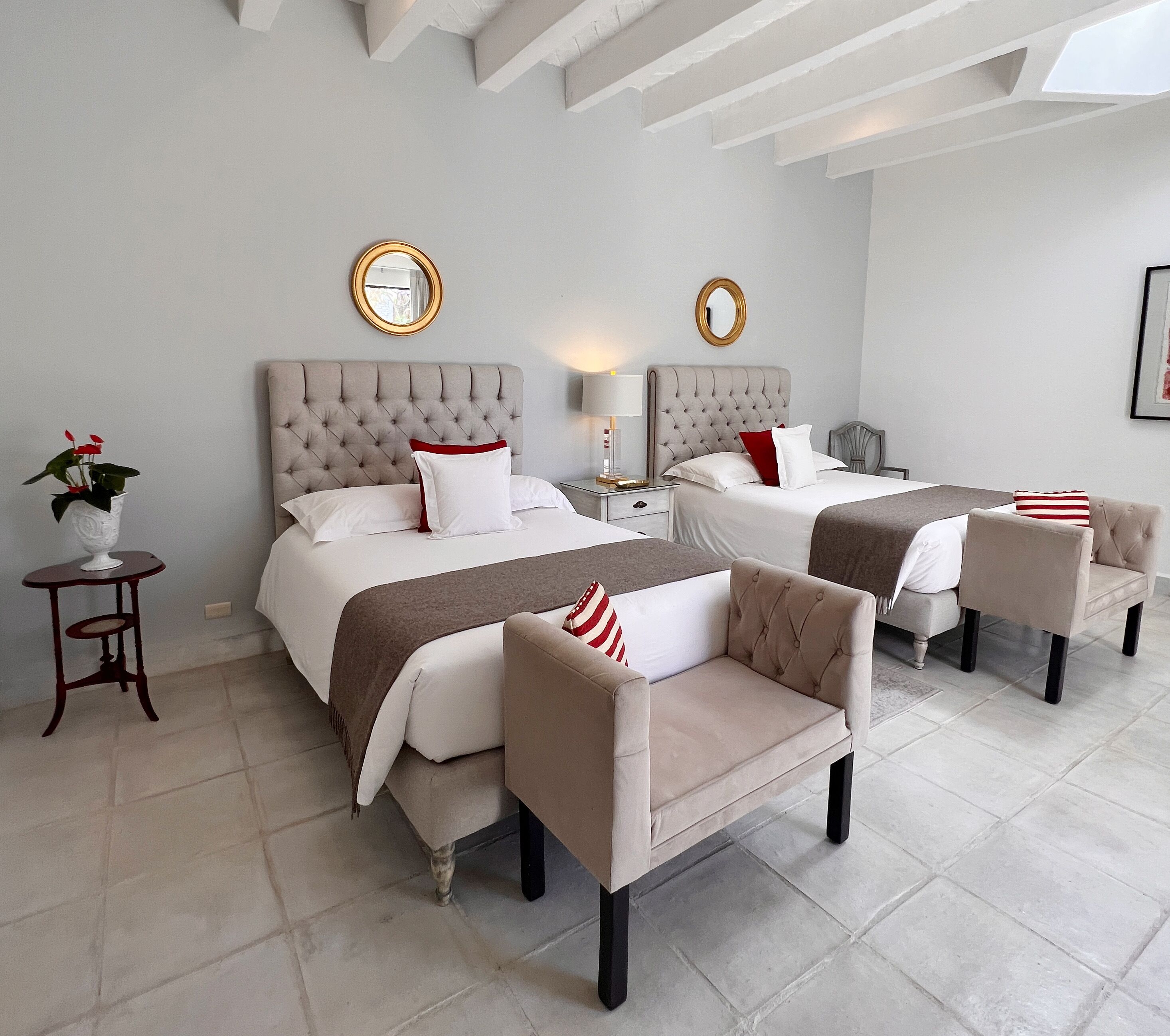Habitación de hotel con dos camas, un área de descanso con sillas, una mesita con una planta y un espejo montado en la pared.