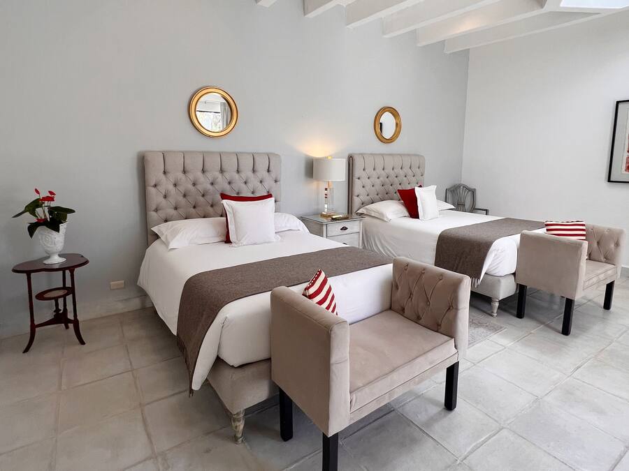 Habitación de hotel con dos camas, un área de descanso con sillas, una mesita con una planta y un espejo montado en la pared.
