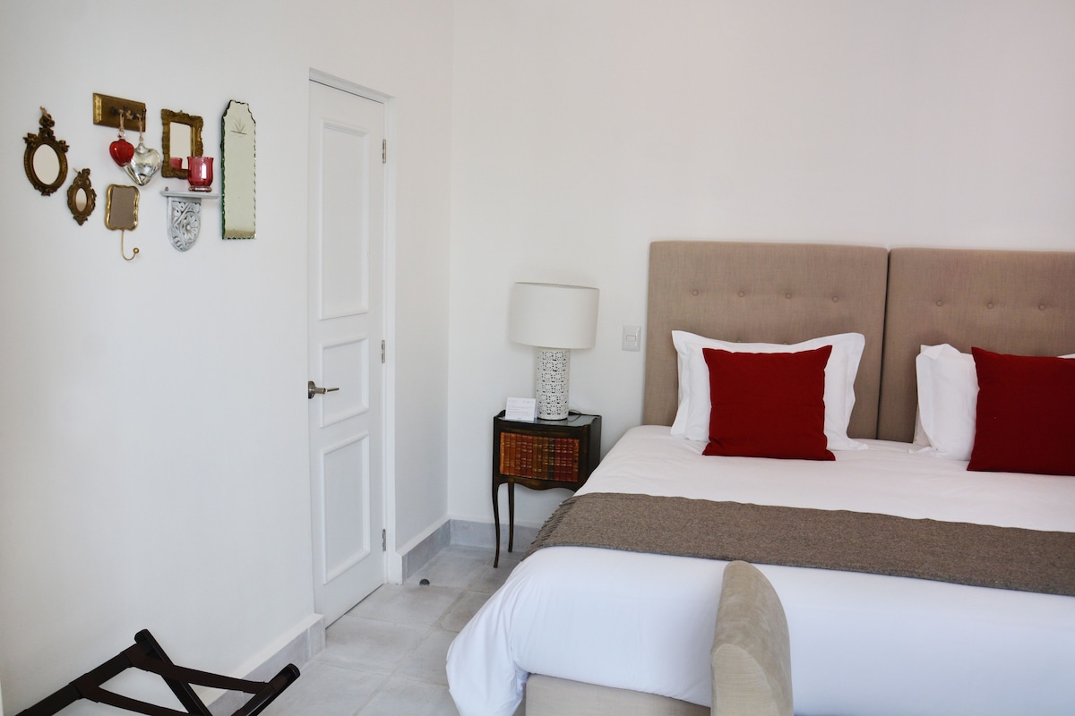 A hotel room with a bed, a nightstand with a lamp, a door, and wall decorations including mirrors and framed pictures.