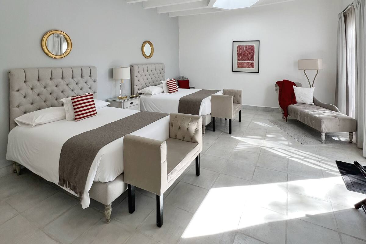 A hotel room with two beds, a sofa, a chair, a nightstand, a lamp, and a window with curtains.