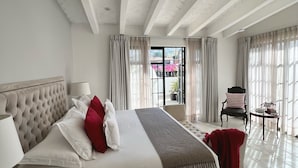 A spacious bedroom with a large bed, a bedside table, a chair, and a view of the outdoors.
