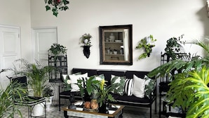 A living room with a patterned floor, a black sofa, and various potted plants.