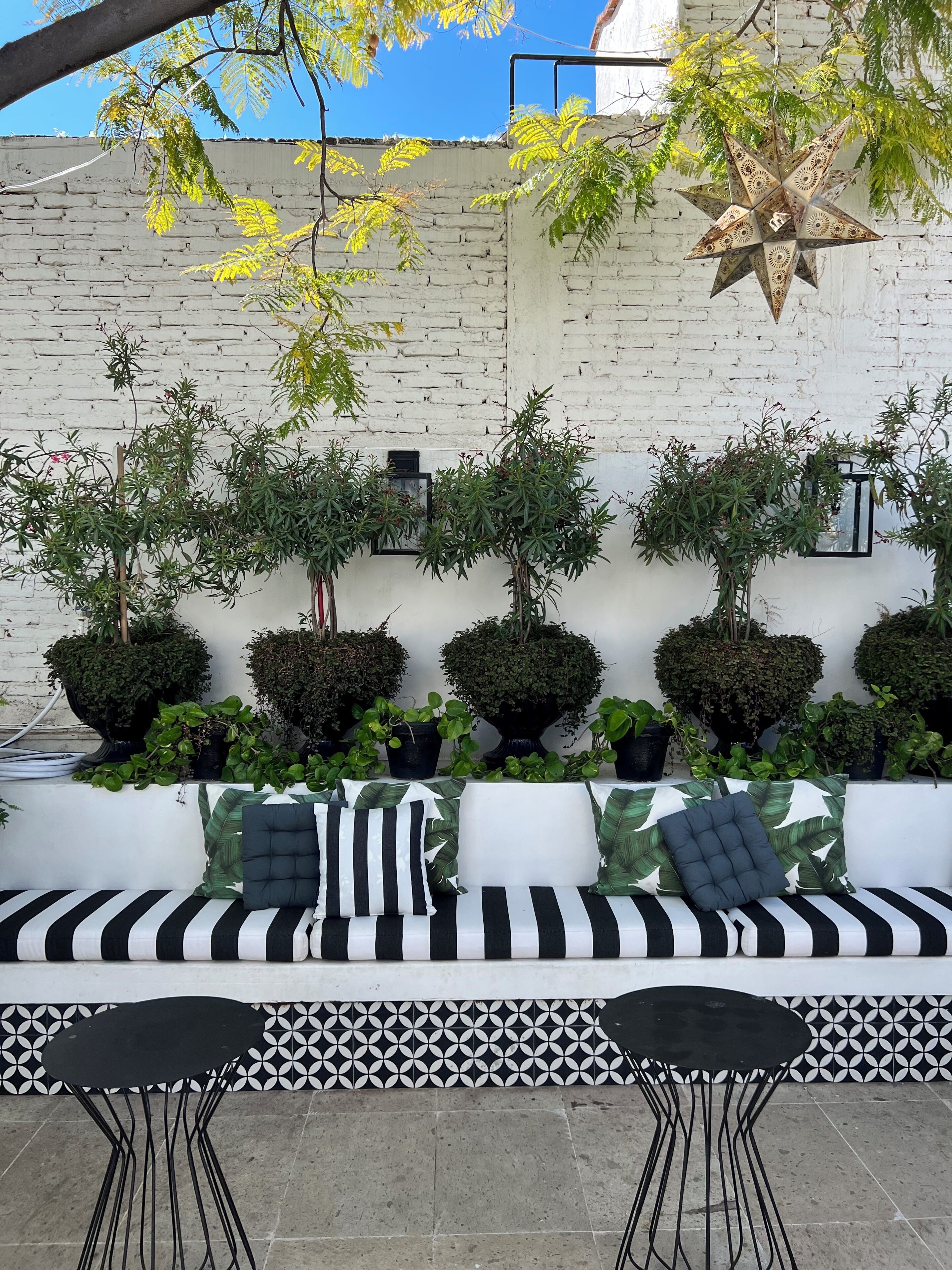 A patio area with a white brick wall, a black and white striped sofa, and multiple potted plants.