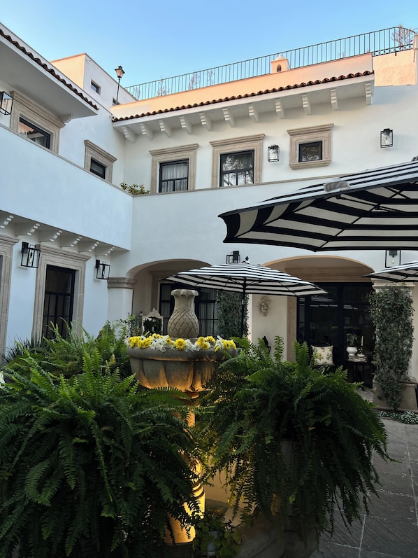 A courtyard with a fountain, potted plants, and a covered seating area.