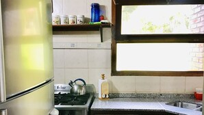A compact kitchen with a refrigerator, stove, and sink. There is a window above the sink, and a shelf with kitchen items. - Casa Chumamaya (Merlo)