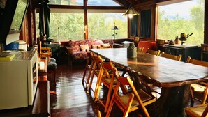 A rustic cabin interior with a wooden dining table, chairs, a sofa, and a kitchen area with a stove. - Casa Chumamaya (Merlo)