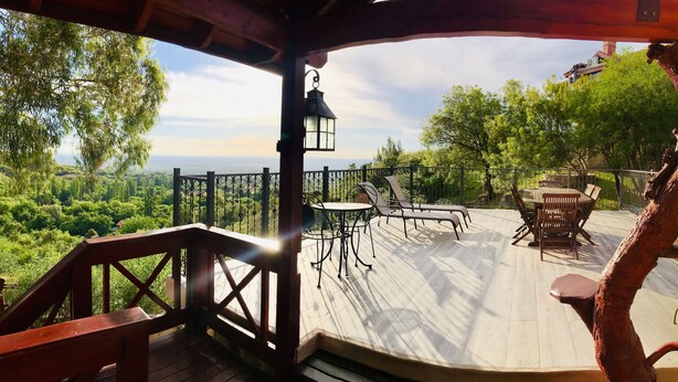 A wooden deck with outdoor furniture, a lantern, and a view of a forested landscape. - Casa Chumamaya (Merlo)