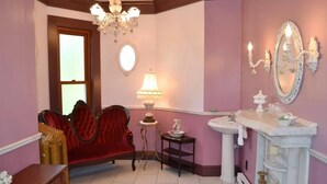 A room with a red velvet sofa, a chandelier, a mirror, and a vanity with a sink. - The Conner House B&B (Prairie du Rocher)