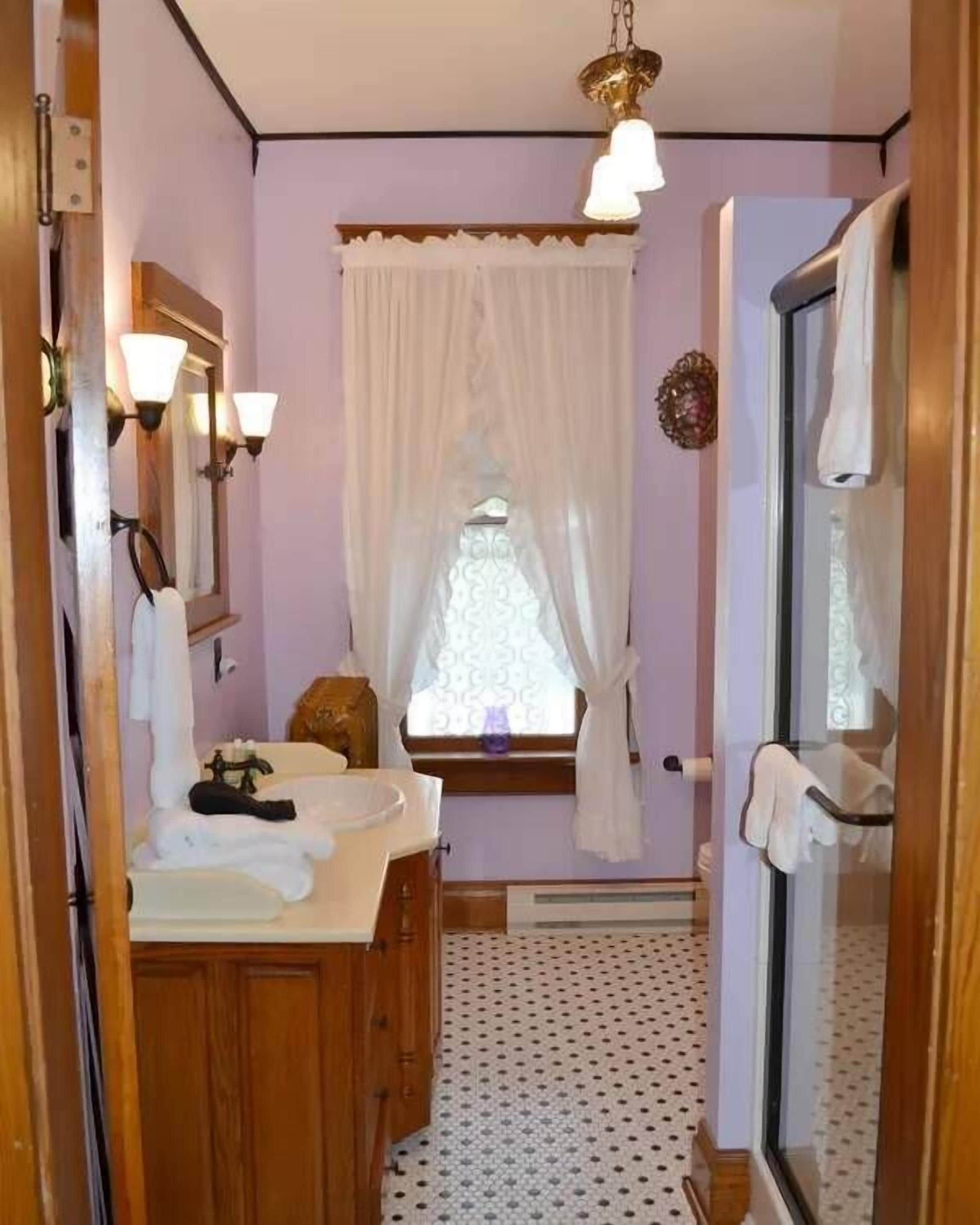A narrow bathroom with a sink, mirror, and window with curtains.