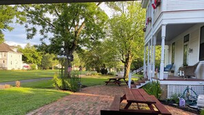 A covered patio with a picnic table, surrounded by a brick pathway and greenery. - The Conner House B&B (Prairie du Rocher)
