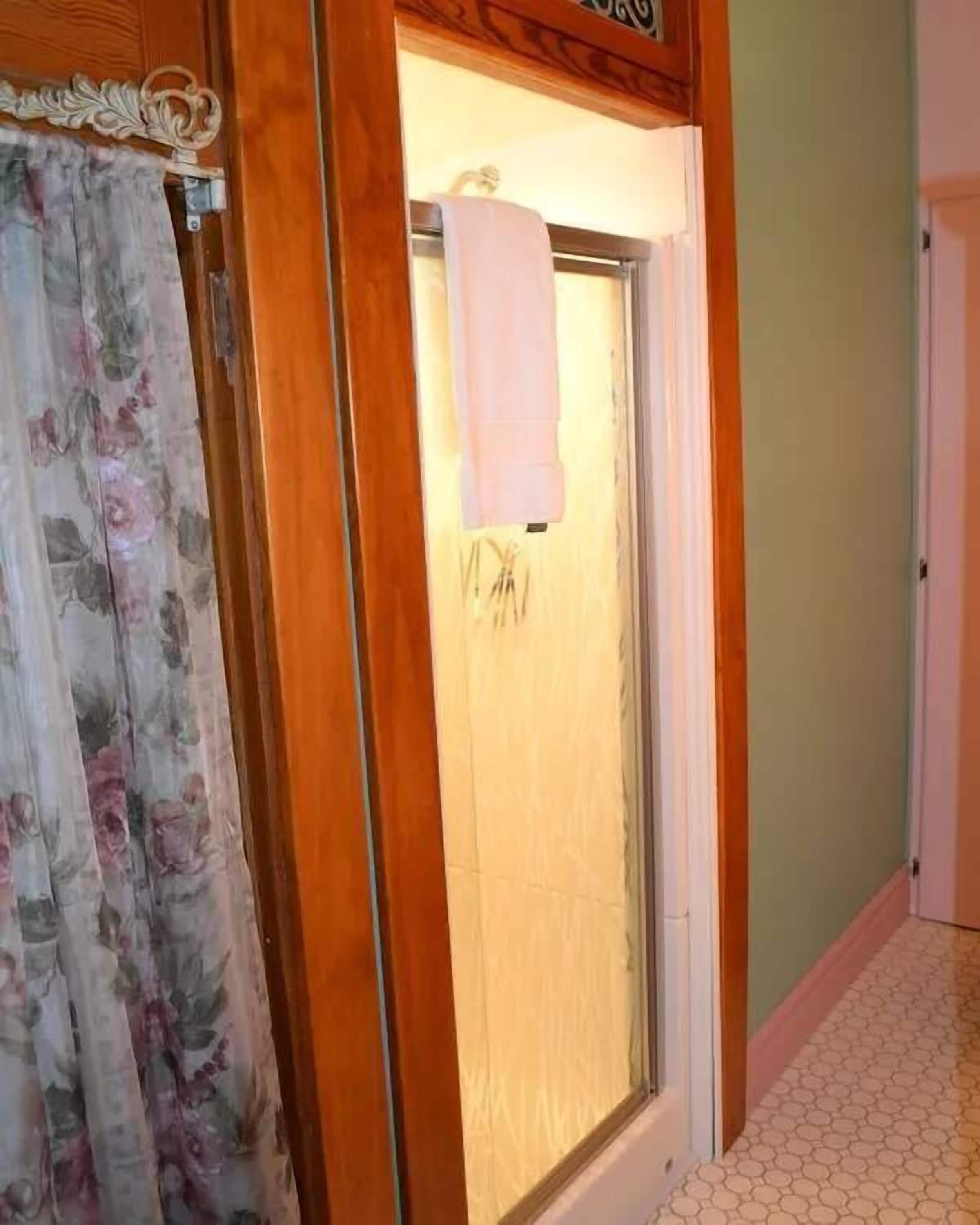 Un baño con ducha, una toalla colgada en la pared y una cortina con motivos florales.