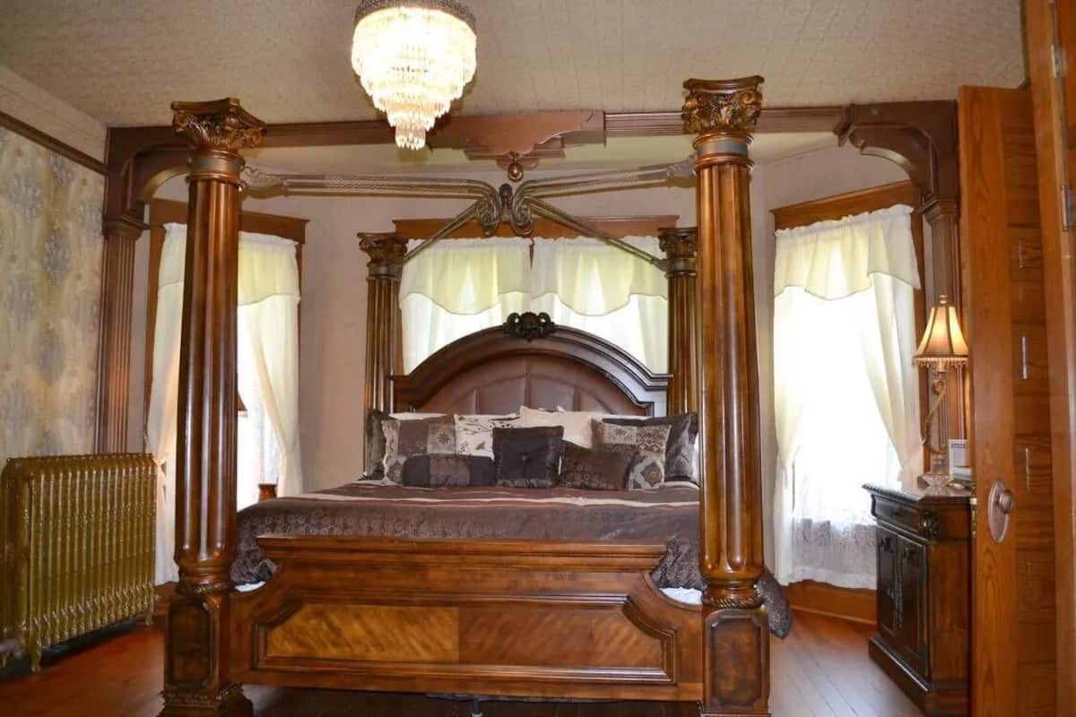 A four-poster canopy bed with a wooden headboard, a chandelier, and a radiator on the floor.