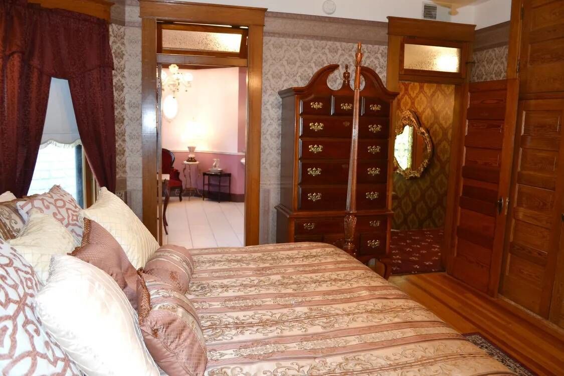 A bedroom with a large bed, wooden wardrobe, and a mirror on the wall.