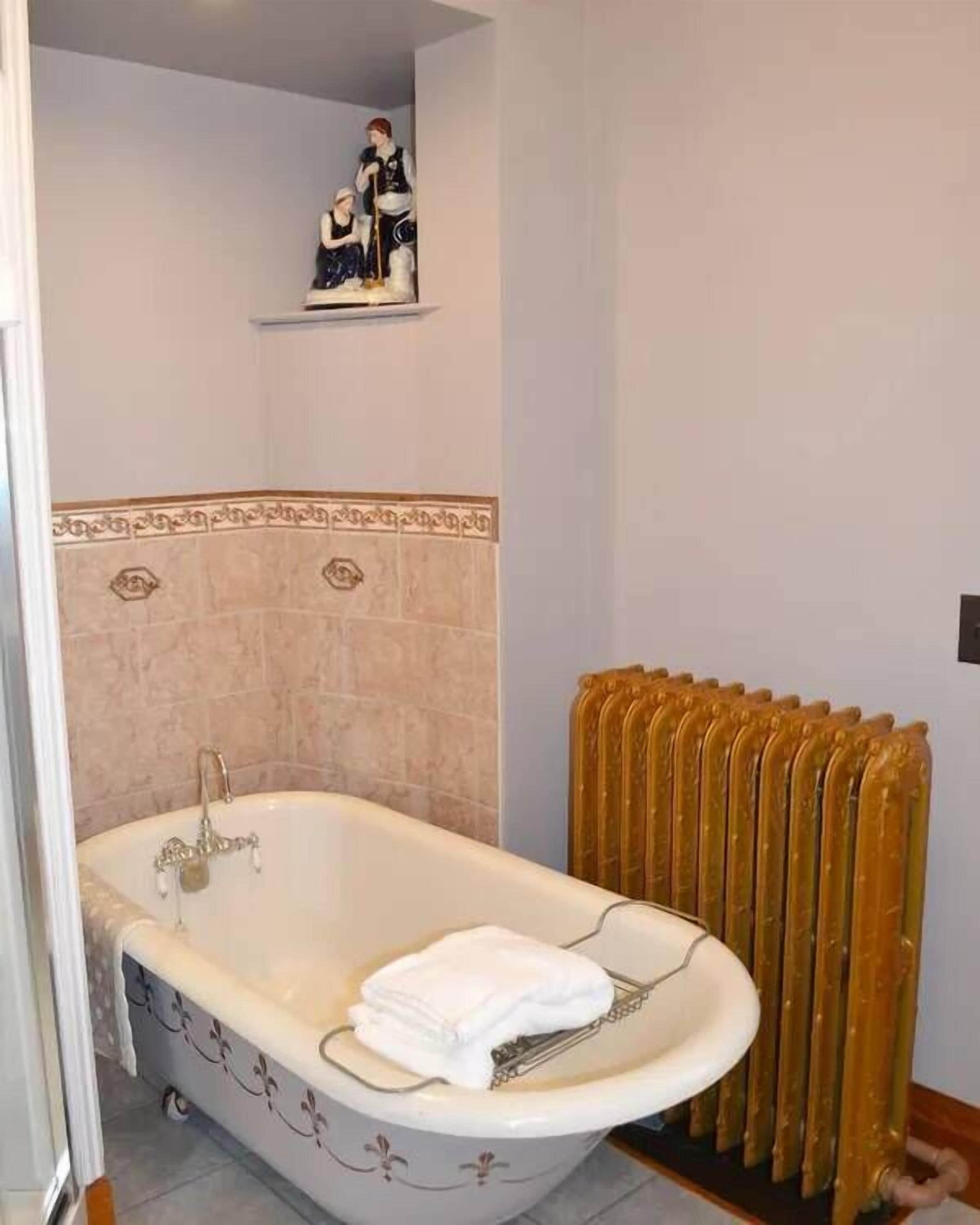 Un baño con una bañera independiente, un radiador y un estante decorativo con figuritas.