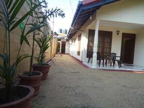 A courtyard with potted plants, a covered seating area with chairs, and a building with a tiled roof and windows. - New Sanmi Resort (Malabe)
