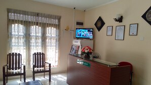 Un área de recepción con un mostrador de madera, dos sillas de madera, un banco, un televisor en la pared y diplomas enmarcados.