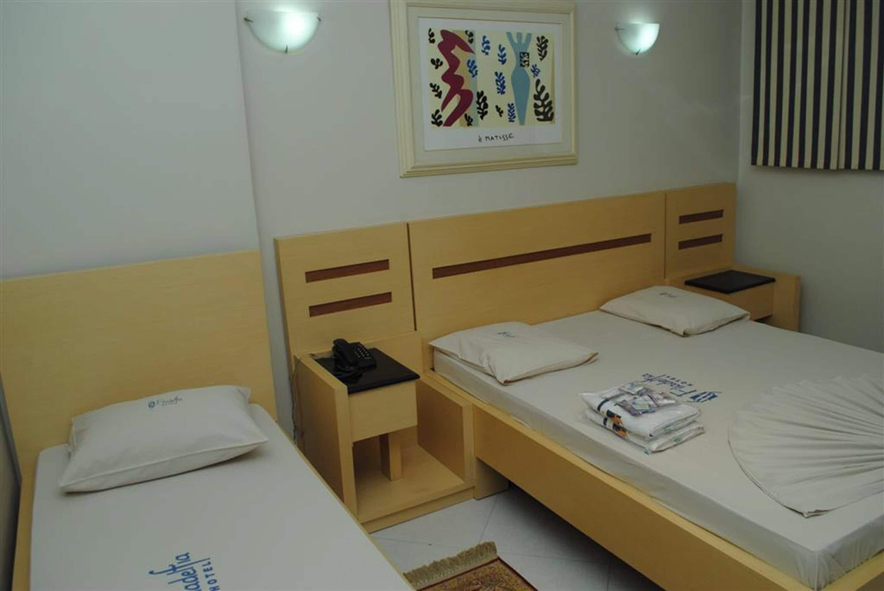 A hotel room with two single beds, a bedside table with a lamp, a framed artwork on the wall, and a striped curtain.
