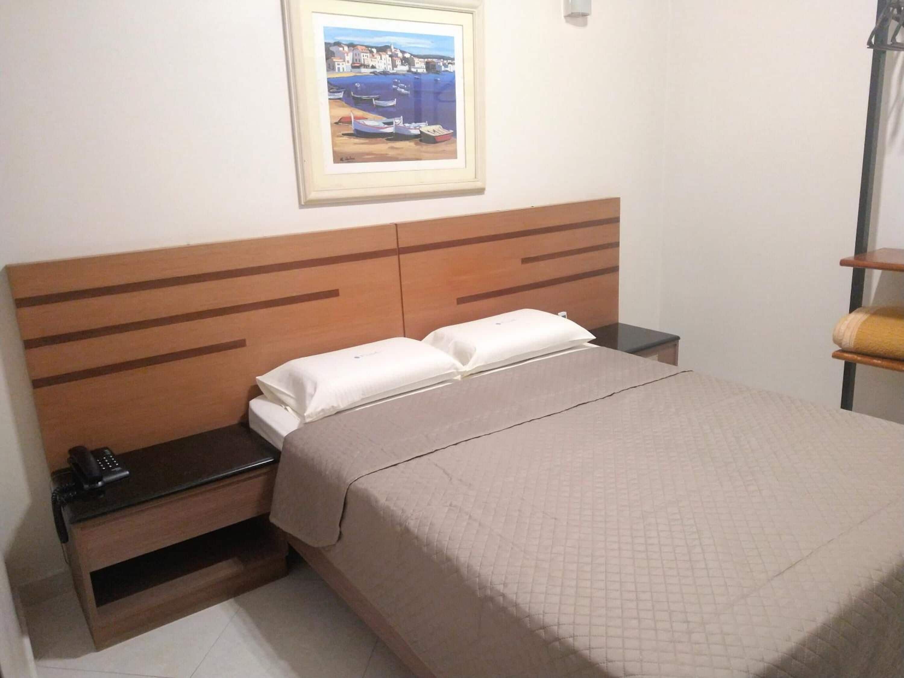 A hotel room with a wooden headboard, a bed with a quilted cover, a bedside table with a phone, and a framed picture on the wall.