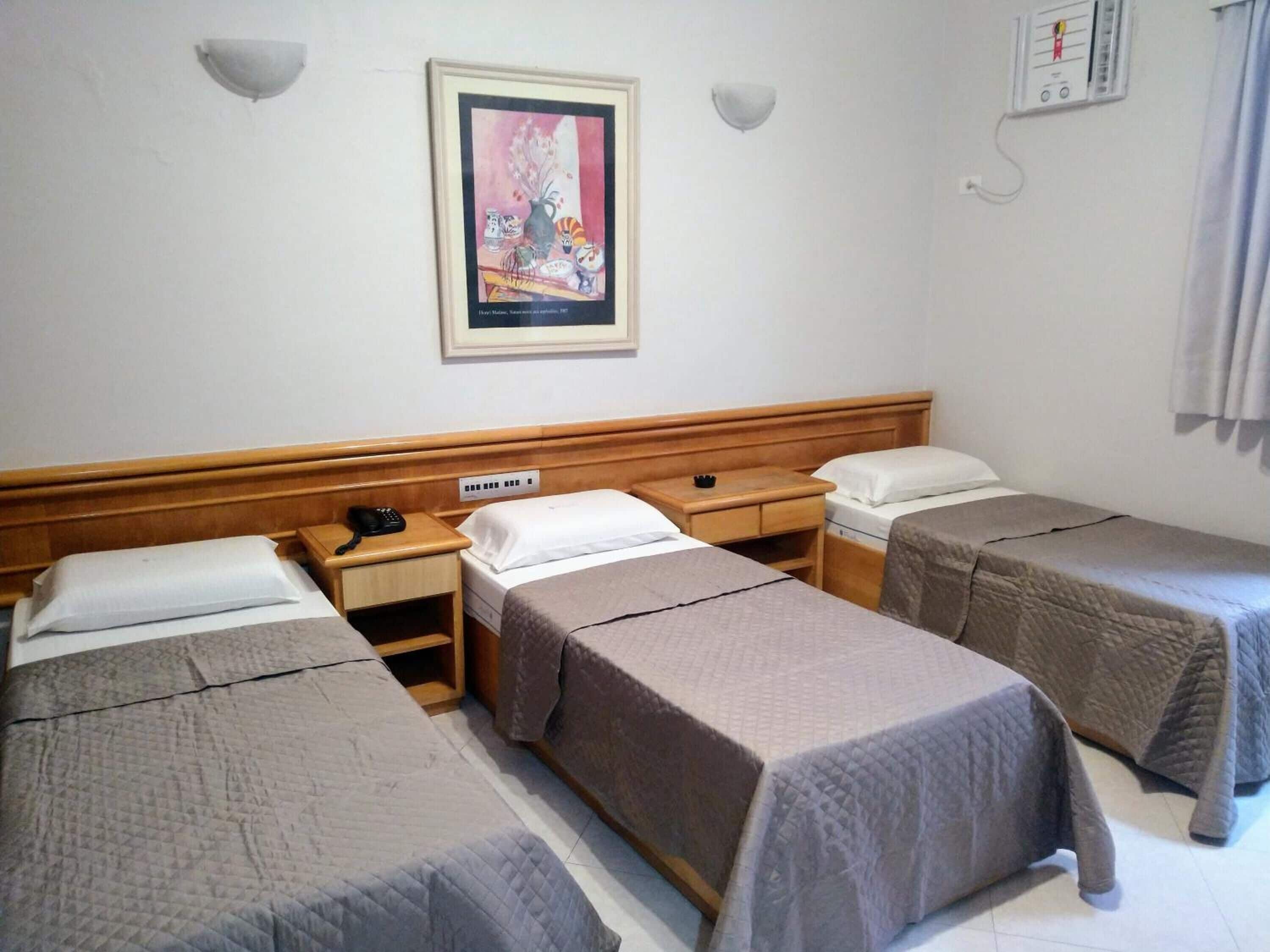 A hotel room with three single beds, a wooden headboard, a bedside table with a phone, and a framed picture on the wall.