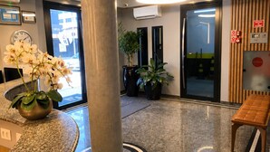 En entréhall med en receptionsdisk, en stor pelare, krukväxter, en bänk och en klocka på väggen.