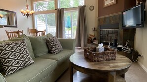 A living room with a green sofa, patterned pillows, a round coffee table, a television, and a fireplace. - Mountain Harbor #204  2 Bedroom Condo (Whitefish)