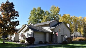 A single-story house with a gabled roof, a front porch, and a small front yard with a lawn and a few shrubs. - Mountain Harbor #204  2 Bedroom Condo (Whitefish)