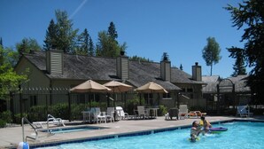 Una piscina con sillas de descanso y sombrillas, rodeada por una cerca y árboles.