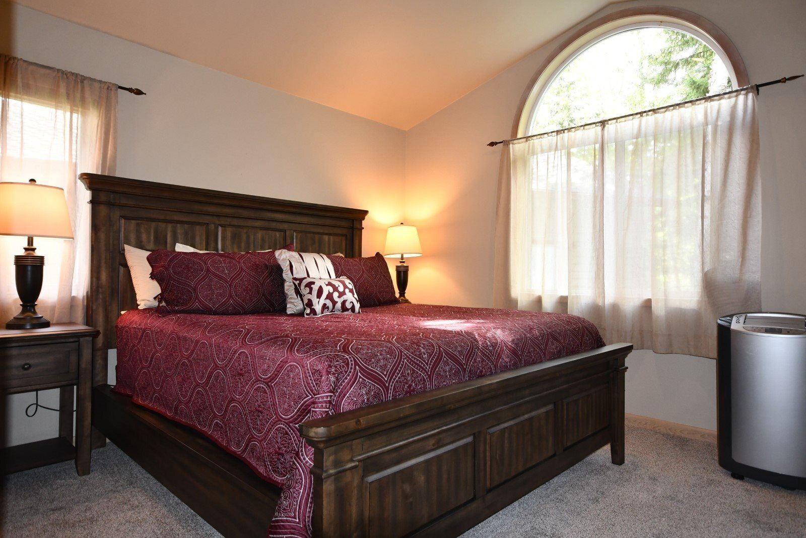 A bedroom with a large bed, two bedside lamps, a window with a view, and a trash can.