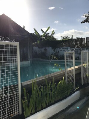 Une piscine entourée d’une clôture en métal, avec de la verdure tout autour et une clôture en bois en arrière-plan.
