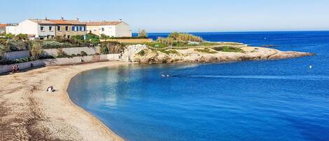 A coastal property with a beach, clear blue water, and a house with a red roof.