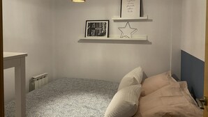 Une chambre avec une couvre-lit à motifs, un luminaire suspendu et des étagères murales ornées de tableaux encadrés et d’une décoration en forme d’étoile.