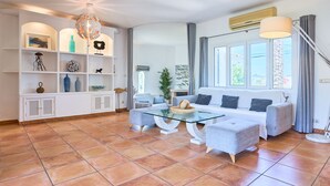 Ein geräumiges Wohnzimmer mit einem Glastisch, grauen Sofas und einer weißen Regaleinrichtung mit Dekorationselementen.