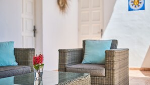 Ein Zimmer mit Korbmöbeln, einem Glastisch und einer Vase mit roten Blumen.