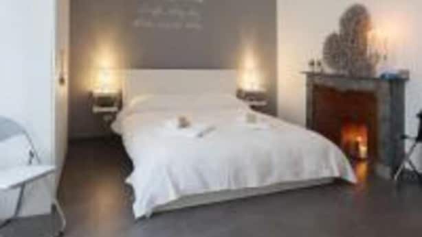 Une chambre à coucher moderne avec un grand lit, deux lampes de chevet, un luminaire fixé au mur et une cheminée.