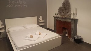 Une chambre avec un grand lit, un mur décoratif orné de motifs, une cheminée et une petite plante.