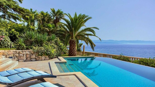 Una piscina infinita con vistas despejadas al mar, rodeada de vegetación exuberante y un muro de piedra.