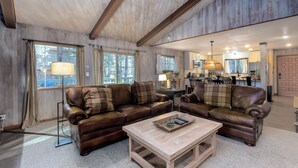 Ein geräumiges Wohnzimmer mit zwei braunen Ledersofas, einem Holztisch und einem Essbereich im Hintergrund.
