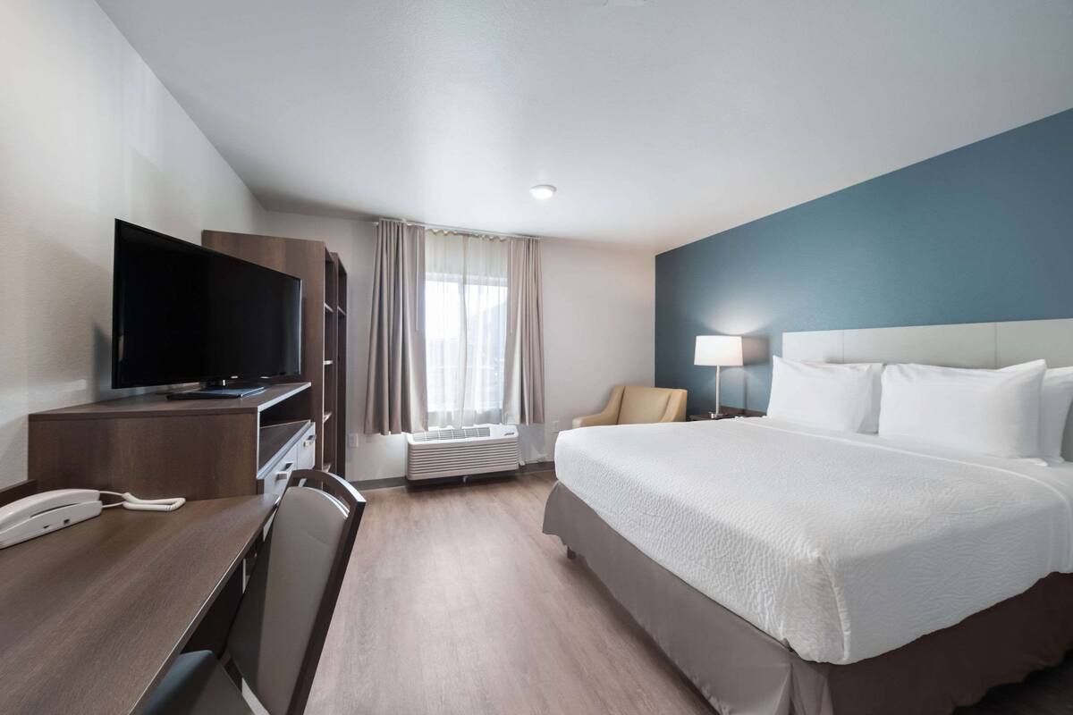 A hotel room with a bed, a desk with a telephone, a television, a chair, a lamp, and a window with curtains.