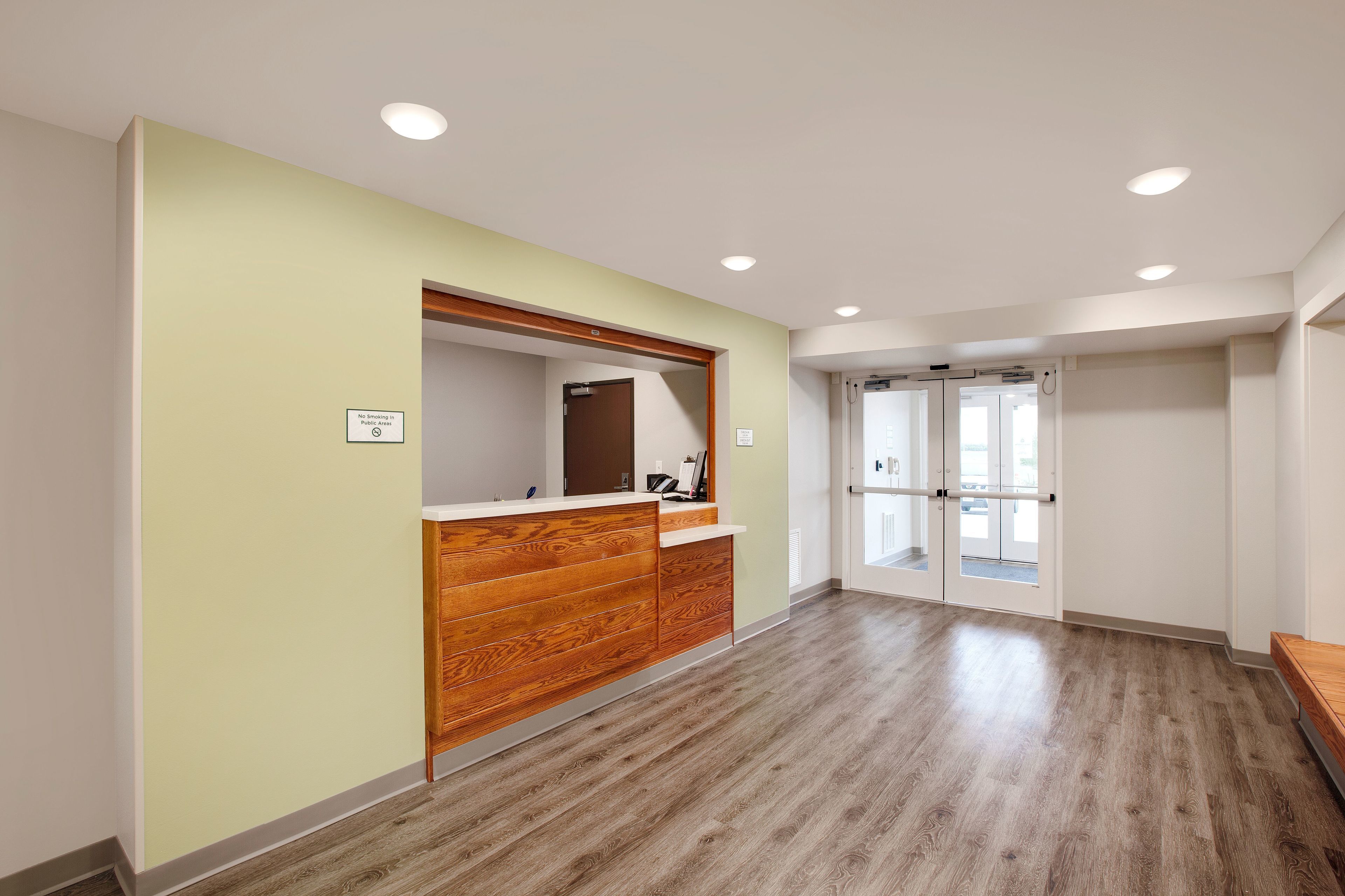 A hallway with a reception desk, wooden paneling, and a glass door entrance.