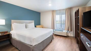 Habitación de hotel con cama, mesita de noche, televisor, ventana con cortinas y aire acondicionado integrado.