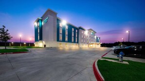 A modern hotel with a flat roof, multiple entry points, and a well-lit exterior. - WoodSpring Suites Dallas Plano Central Legacy Drive (Plano)