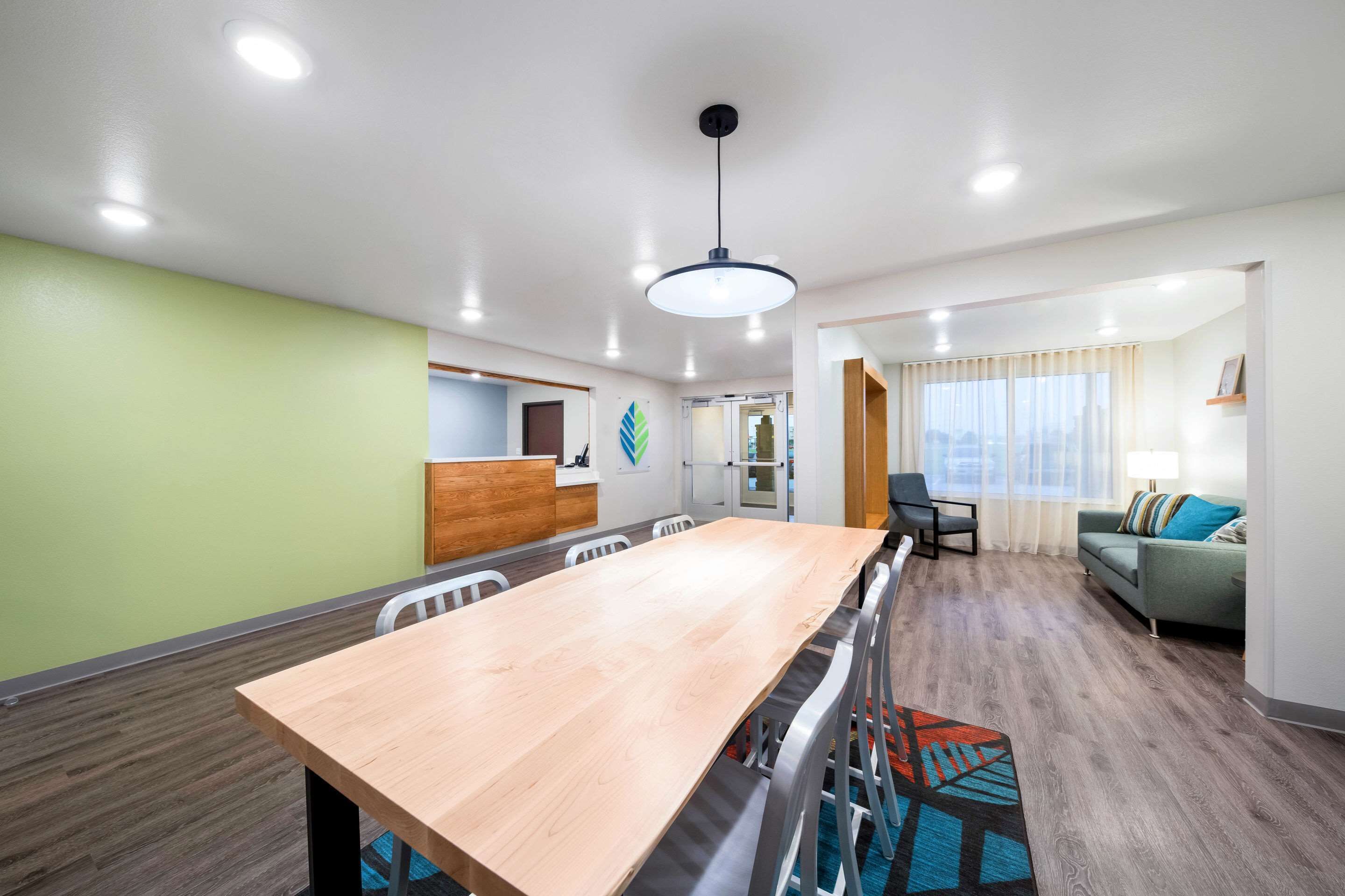 A modern hotel room with a wooden dining table, a sofa, and a kitchen area.