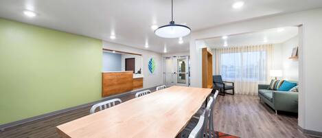 A modern hotel room with a wooden dining table, a sofa, and a kitchen area.