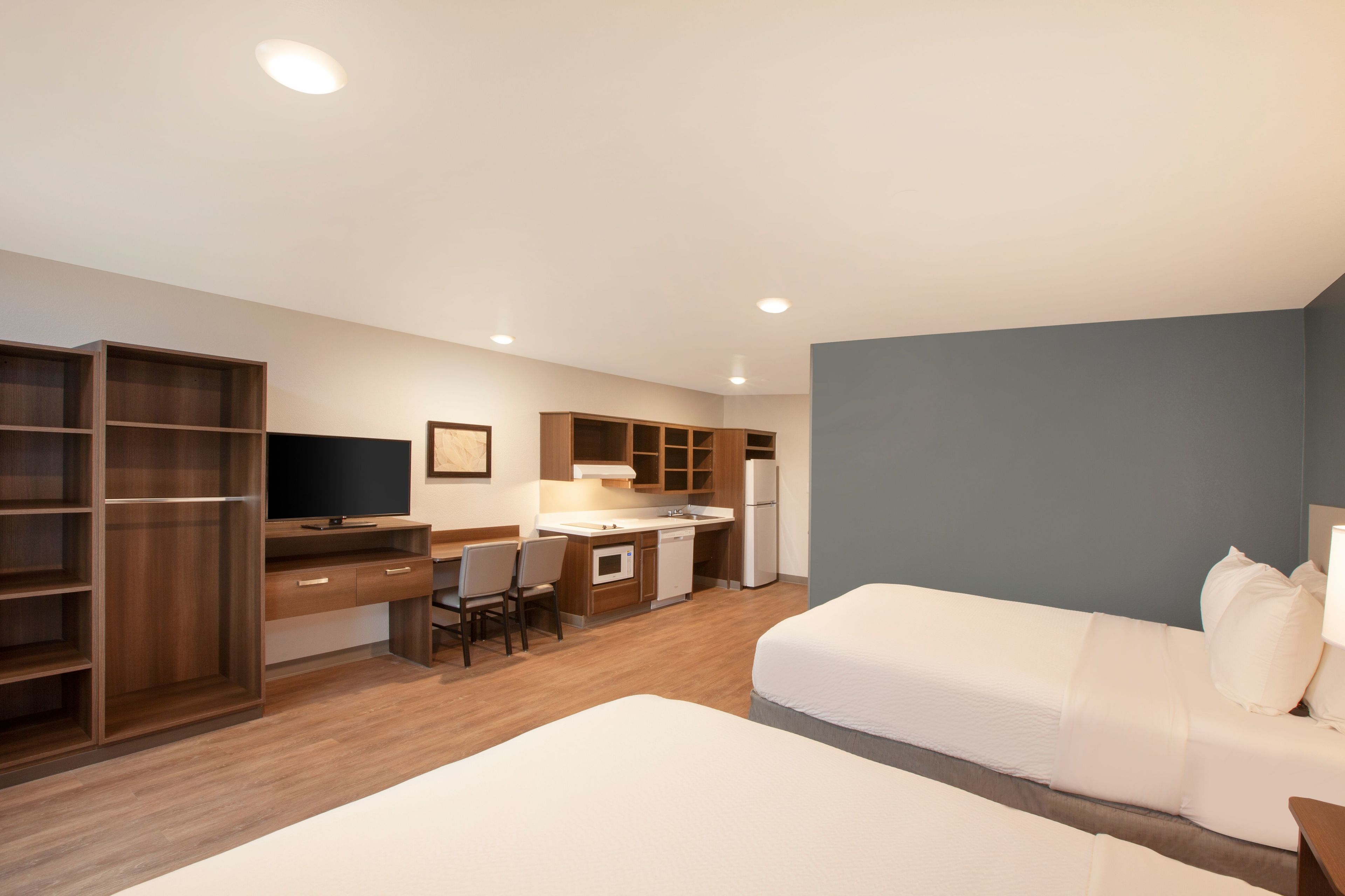 A compact hotel room with a kitchenette, a bed, a desk, and a TV.