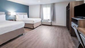 A hotel room with two beds, a TV, a desk, and a window with curtains. - WoodSpring Suites Dallas Plano Central Legacy Drive (Plano)